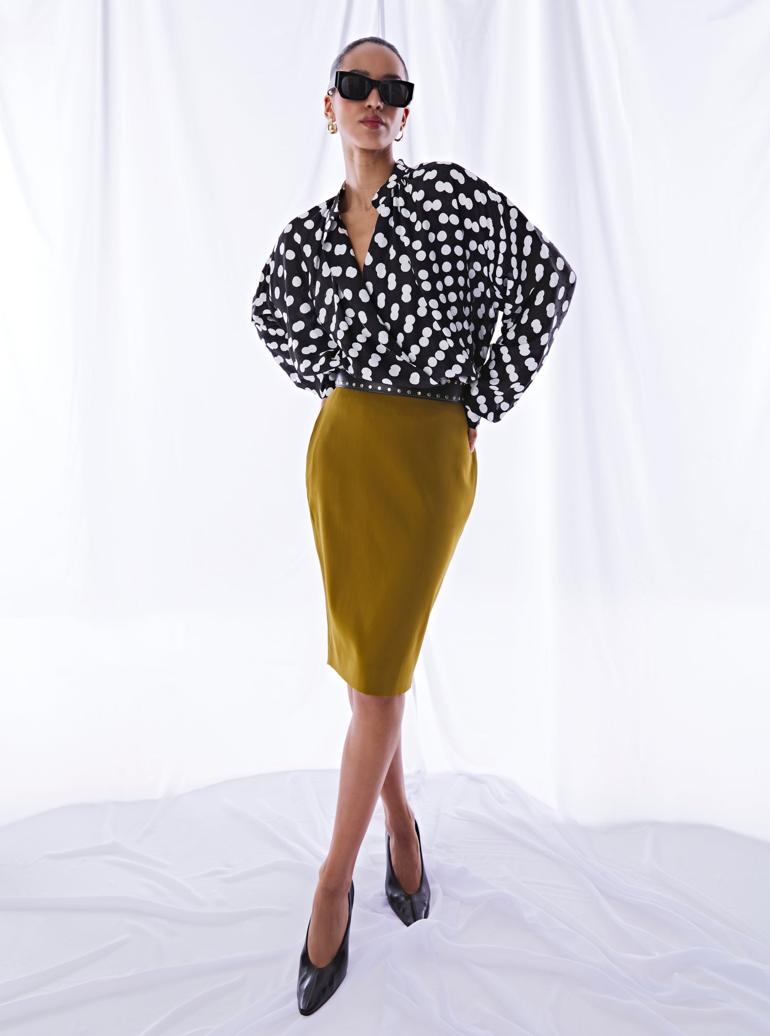 Person wearing a black and white polka dot blouse with a yellow pencil skirt on a white background