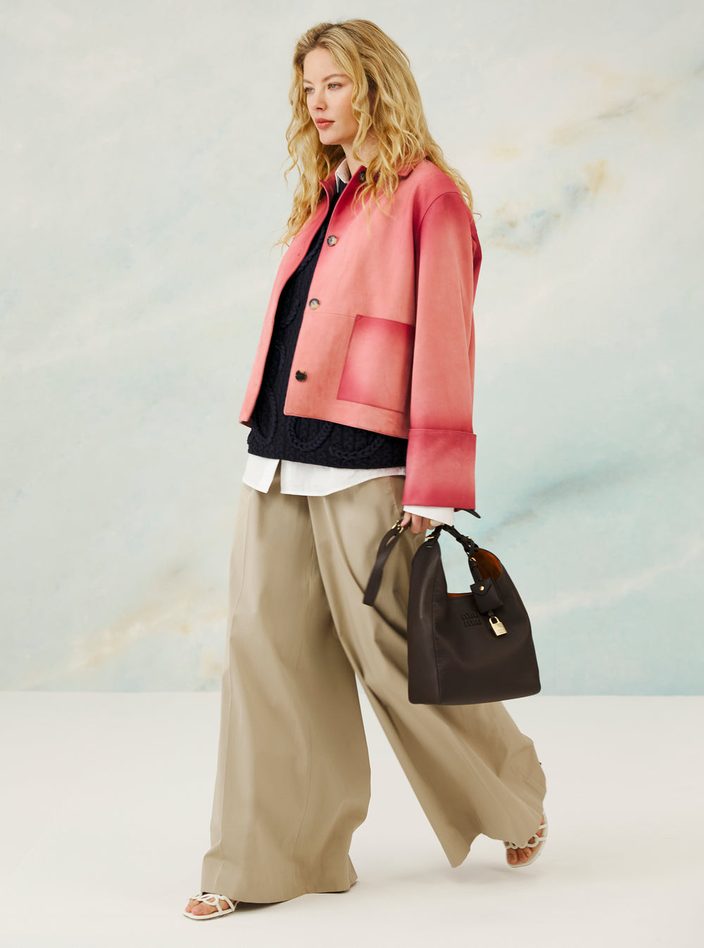 Woman wearing a pink jacket with a black bag on a light background, holding a brown bag