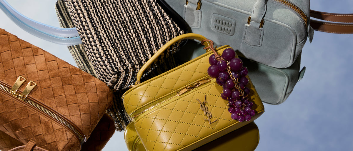 Collection of handbags including a yellow quilted bag, a brown woven bag, and a gray backpack with grapes on a reflective surface.