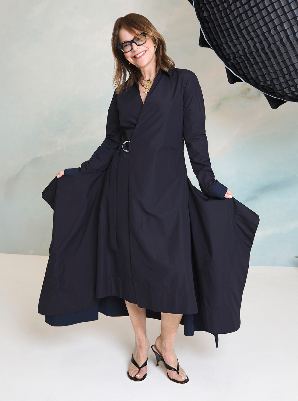 Woman wearing a long navy dress with a belt, standing against a light background.