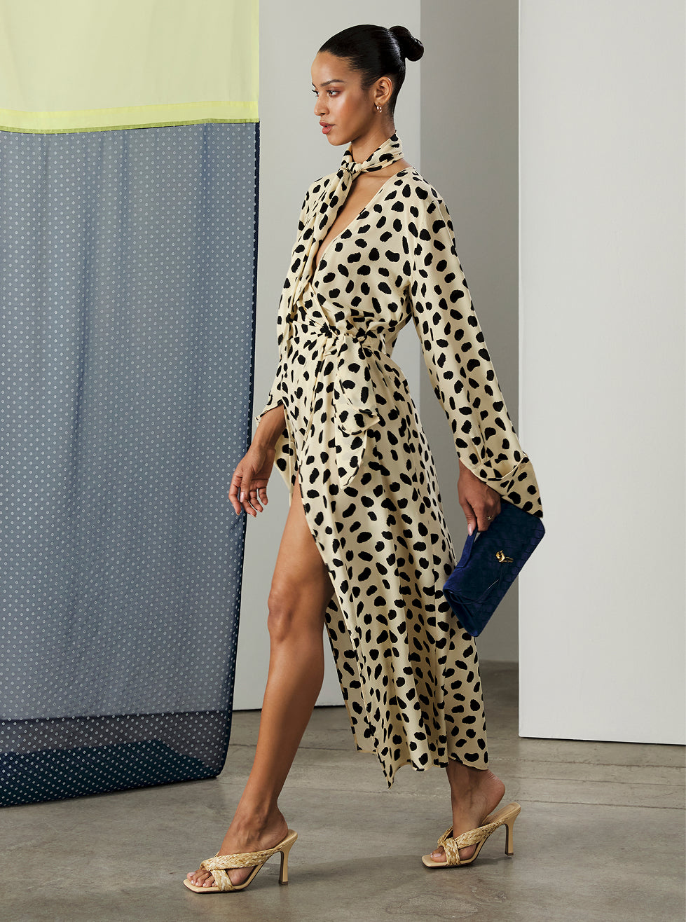 Woman in a leopard print dress holding a blue clutch against a minimal background
