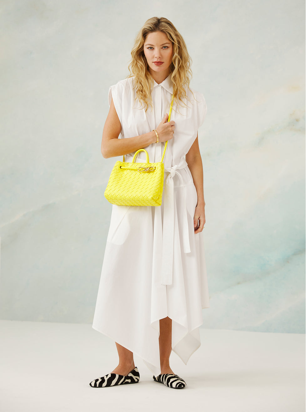 Woman in a white dress holding a yellow handbag against a light background