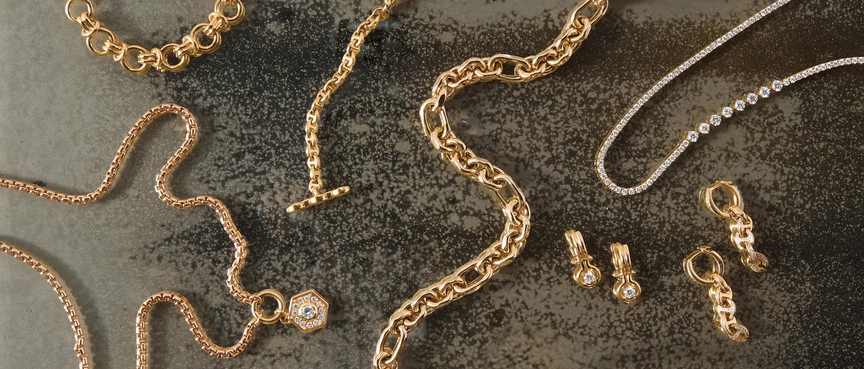 Gold jewelry including necklaces and earrings with diamonds on a textured surface