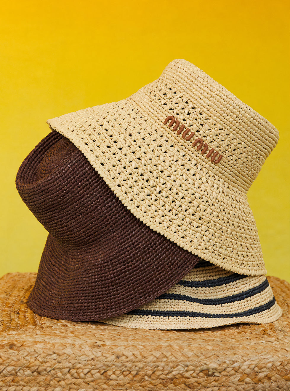 Two woven hats, one beige and one brown, on a textured surface with a yellow background.