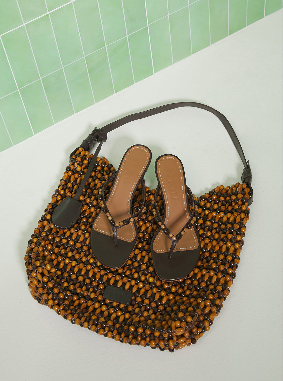 Pair of sandals on a woven mat with a green tiled wall background