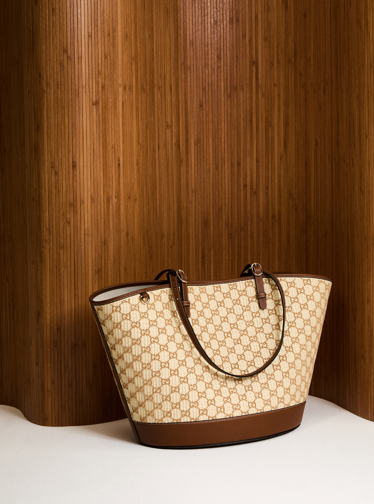Beige and brown patterned handbag on a white surface with a wooden background