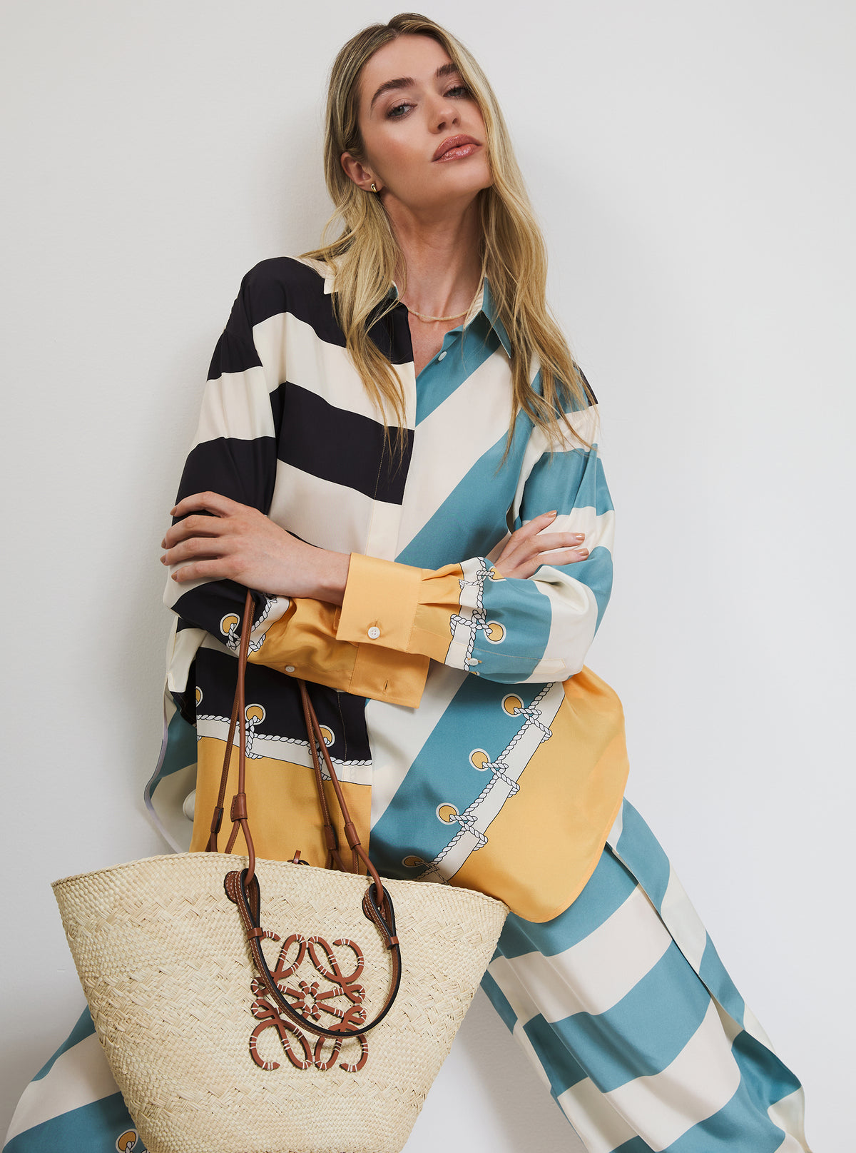 Woman wearing a striped outfit with a yellow bag and straw tote against a white background