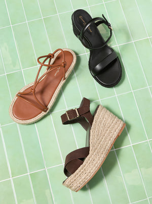 Three pairs of sandals in brown, black, and beige on a green grid background