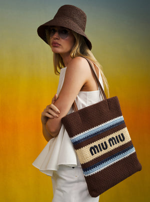 Woman holding a brown Miu Miu tote bag against a gradient background