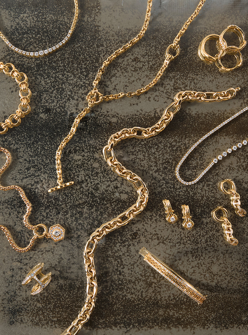 Gold jewelry including necklaces and earrings with diamonds on a textured surface
